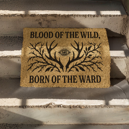 Rectangular coir doormat measuring 24x16 inches featuring black printed text reading “Blood of the Wild, Born of the Ward” with an all-seeing eye symbol and antler-branch illustration. Made from natural coconut fiber with a durable black vinyl backing, this outdoor doormat is weather-resistant and ideal for gothic, witchy, or folklore-inspired entryways.